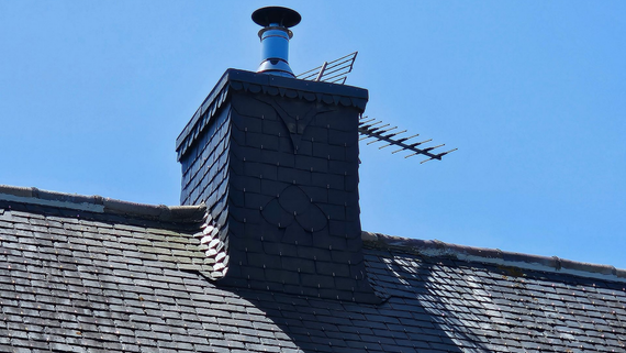 Cheminée avec antenne de télévision et chapeau de cheminée sur un toit en bardeaux, sur fond de ciel bleu.
