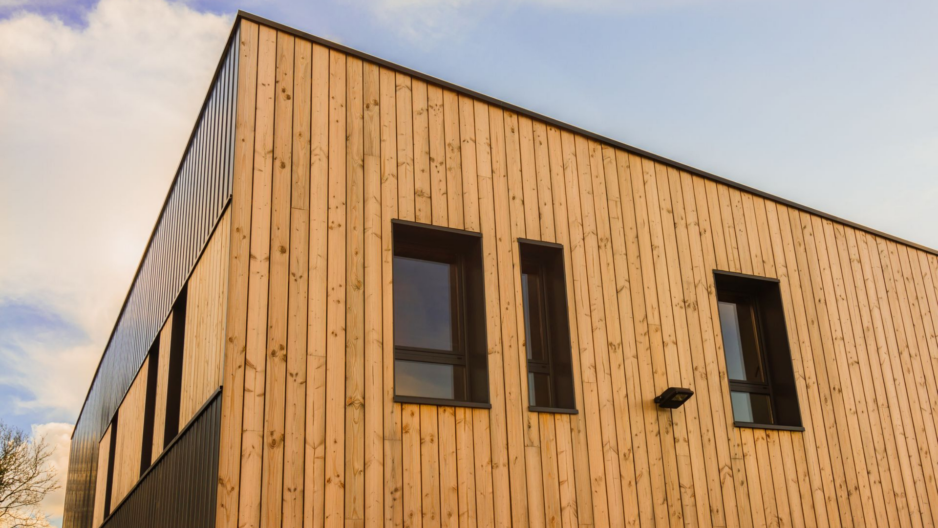 Bâtiment moderne avec bardage en bois et fenêtres à cadre sombre se détachant sur un ciel bleu.