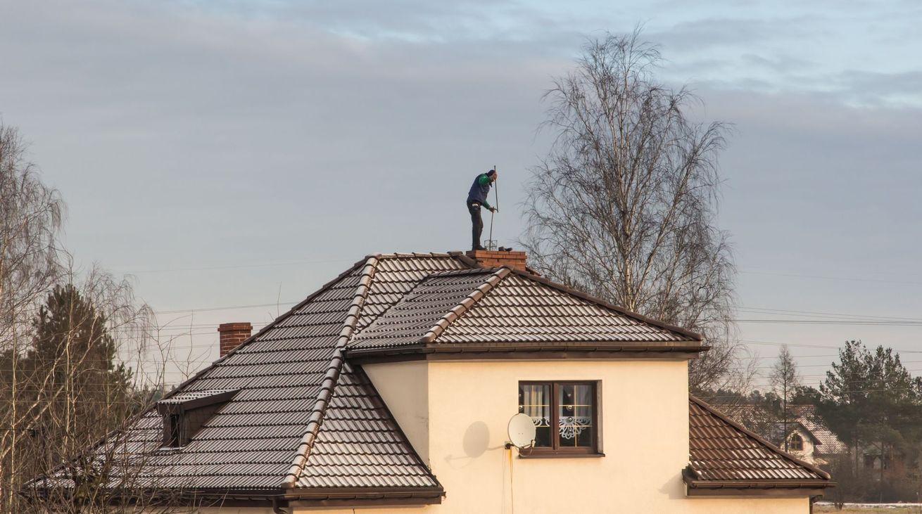 Personne sur un toit, en train de ramoner. Extérieur de la maison, toit enneigé, ciel clair.