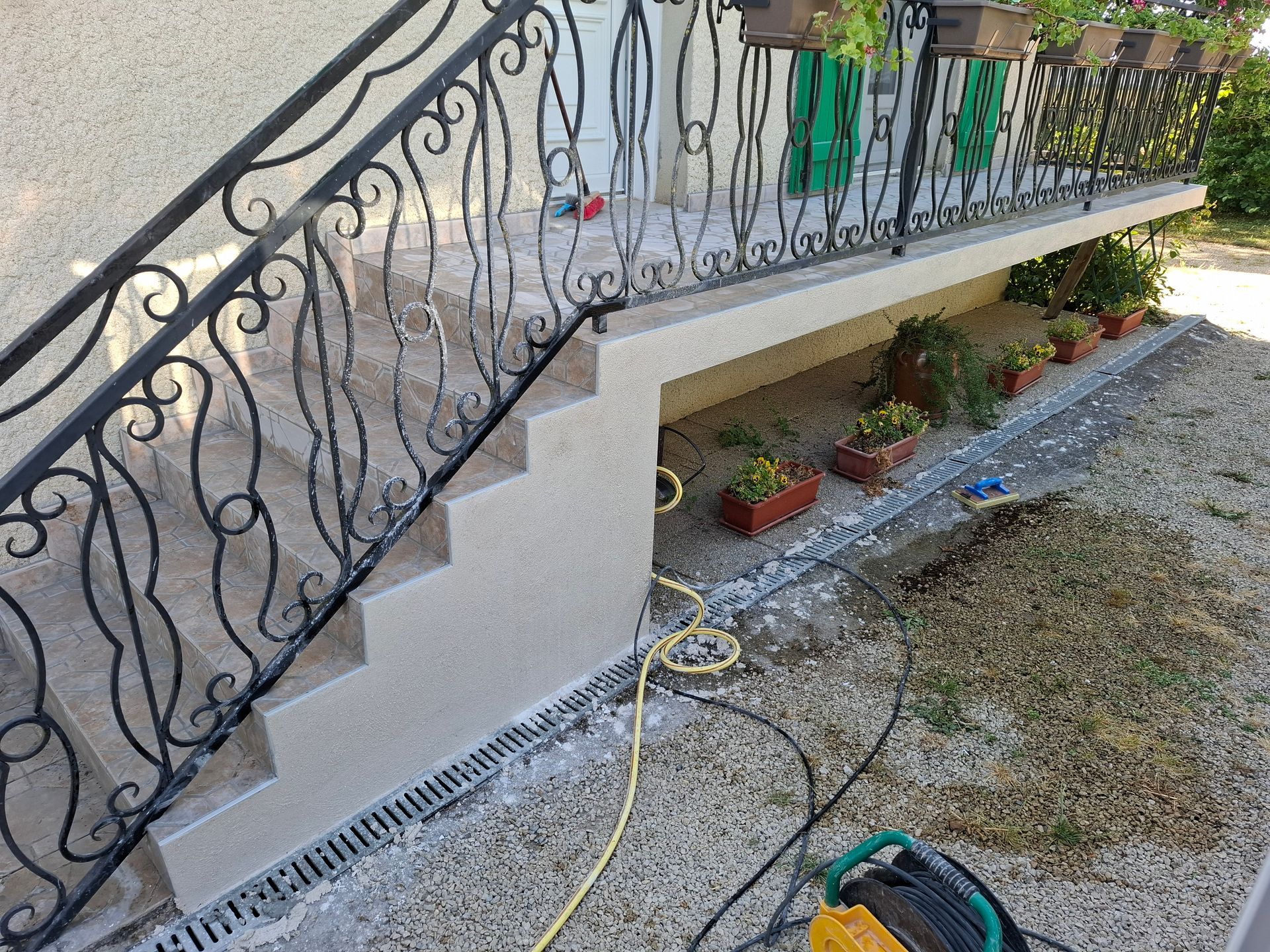 Sol en béton fraîchement coulé dans une pièce aux murs de pierre, avec des tuyaux bleus et rouges apparents.