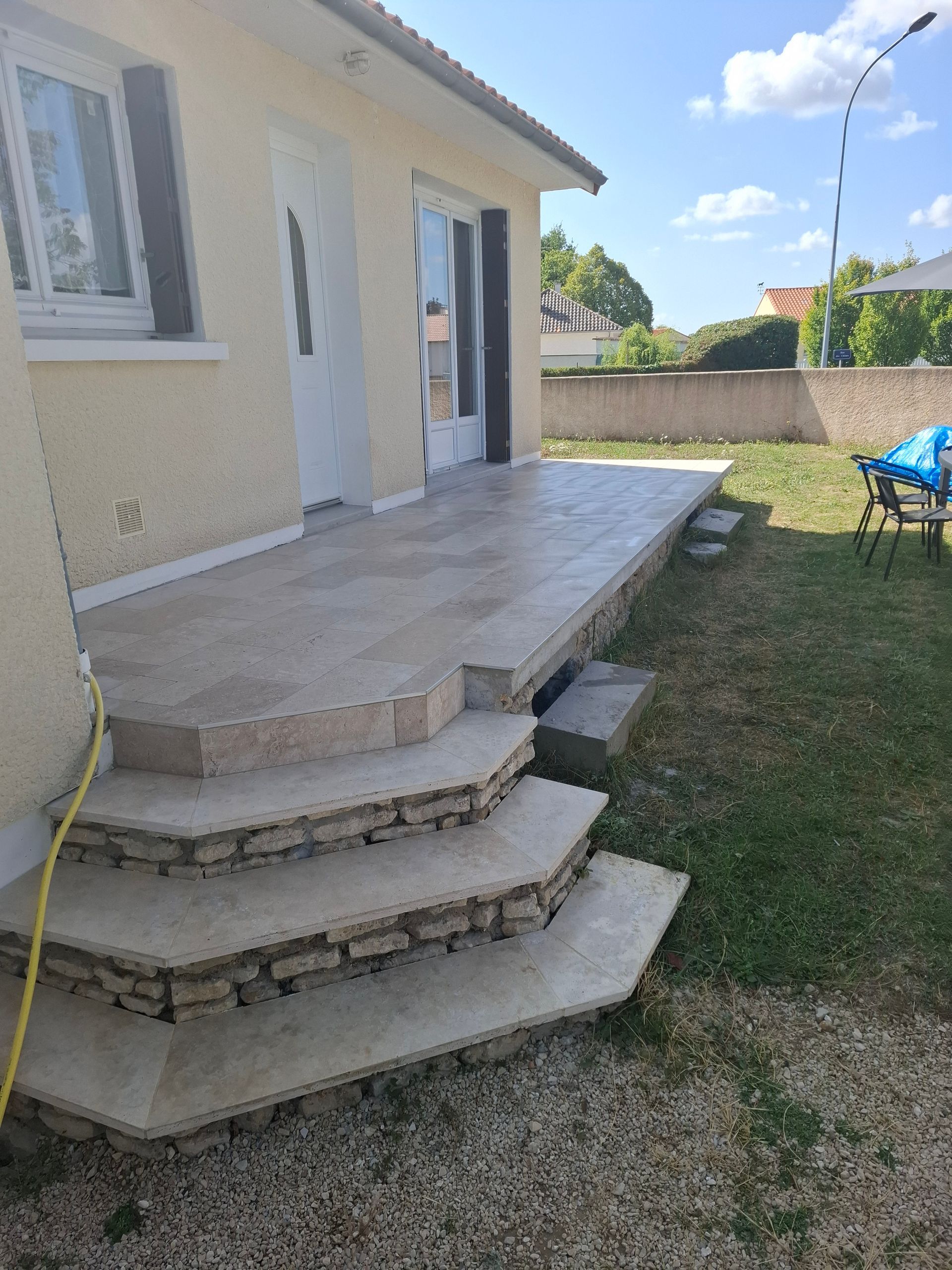 Terrasse en pierre avec des marches menant à une cour gazonnée.