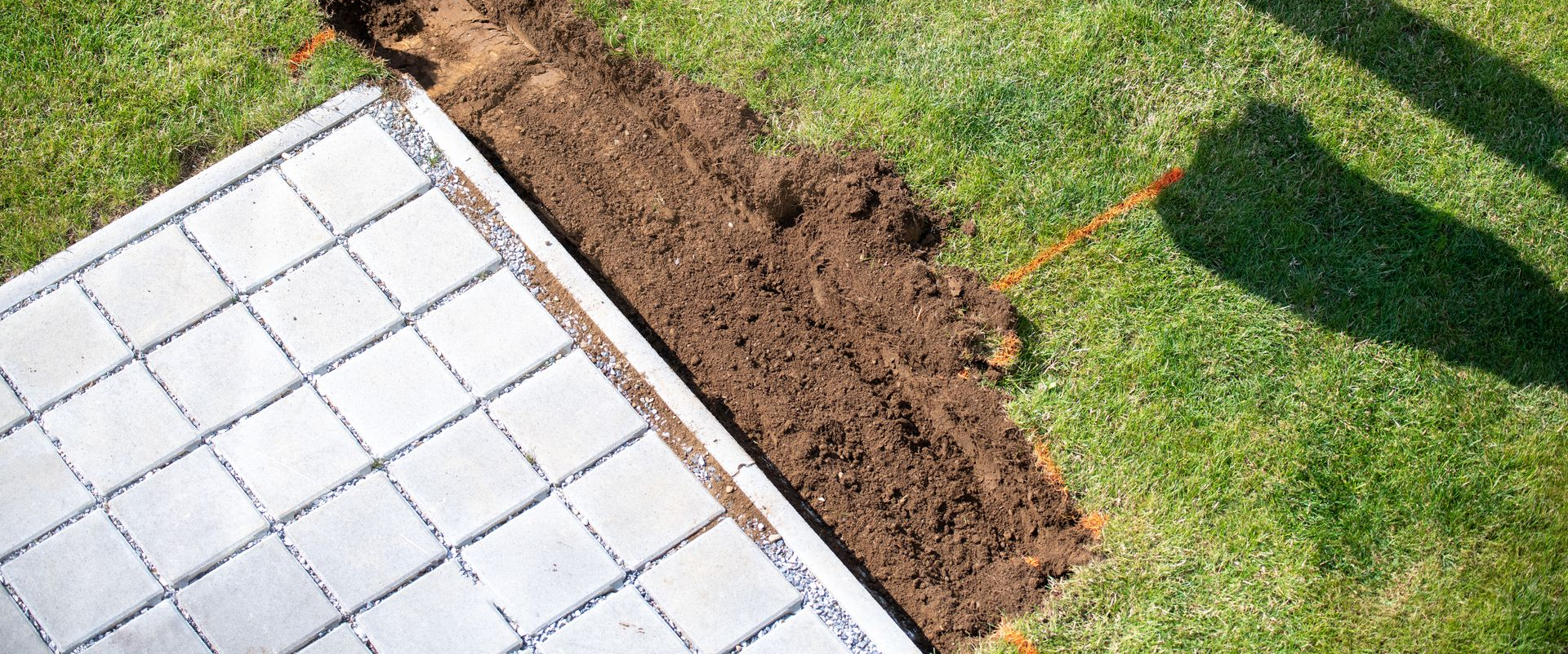Une bordure de terrasse en pierre avec un fossé de terre longeant une pelouse verte.