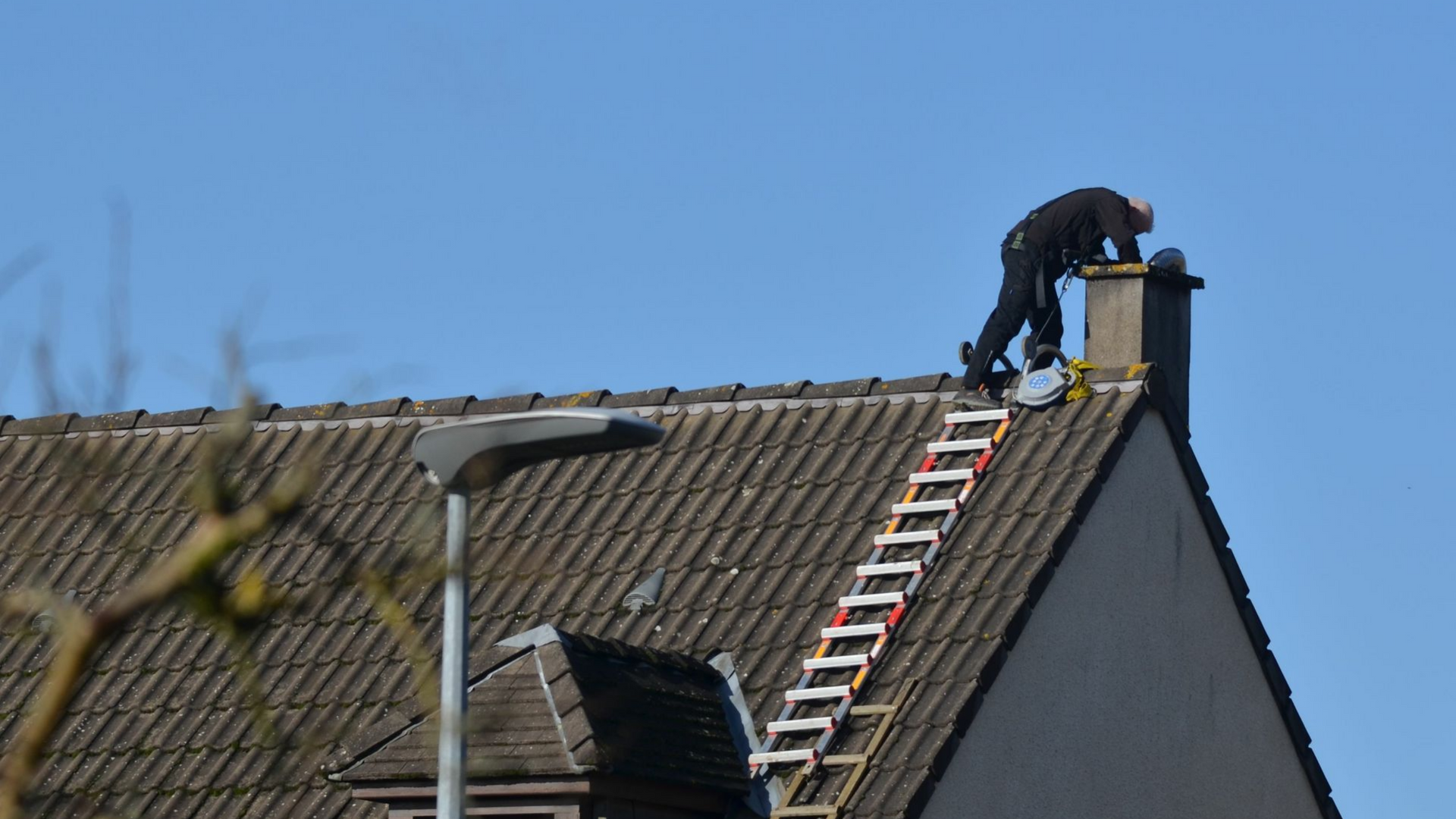 Une personne sur un toit près d'une cheminée, utilisant une échelle par une journée ensoleillée.