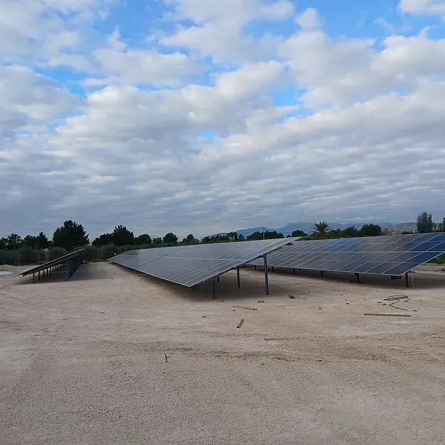 Una fila de paneles solares en un campo de tierra bajo un cielo nublado