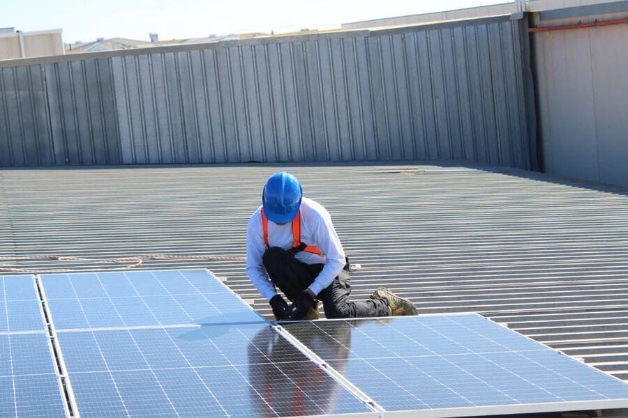 Un hombre está instalando paneles solares en el tejado de un edificio.