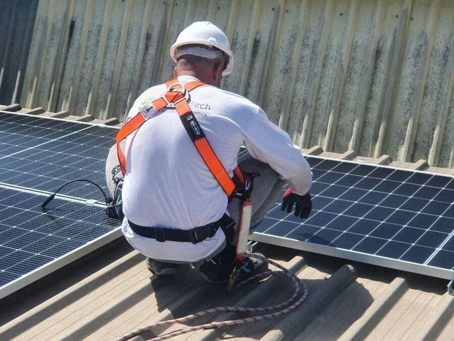 Un hombre está arrodillado sobre un tejado con paneles solares.
