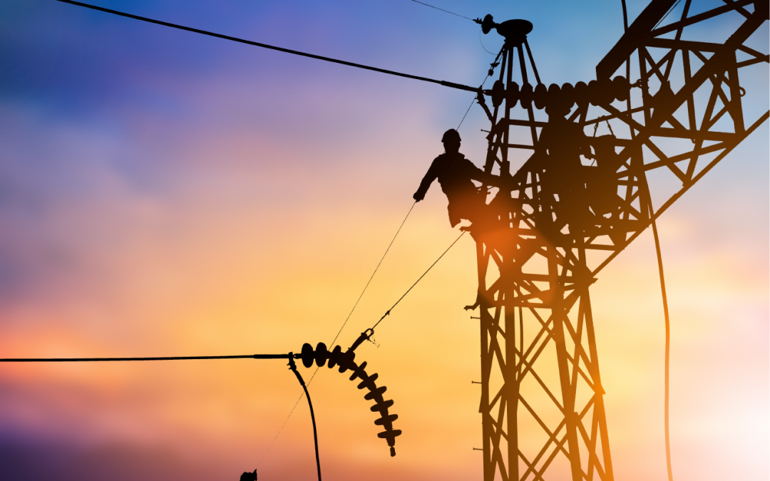 Un hombre está trabajando en una línea eléctrica al atardecer.