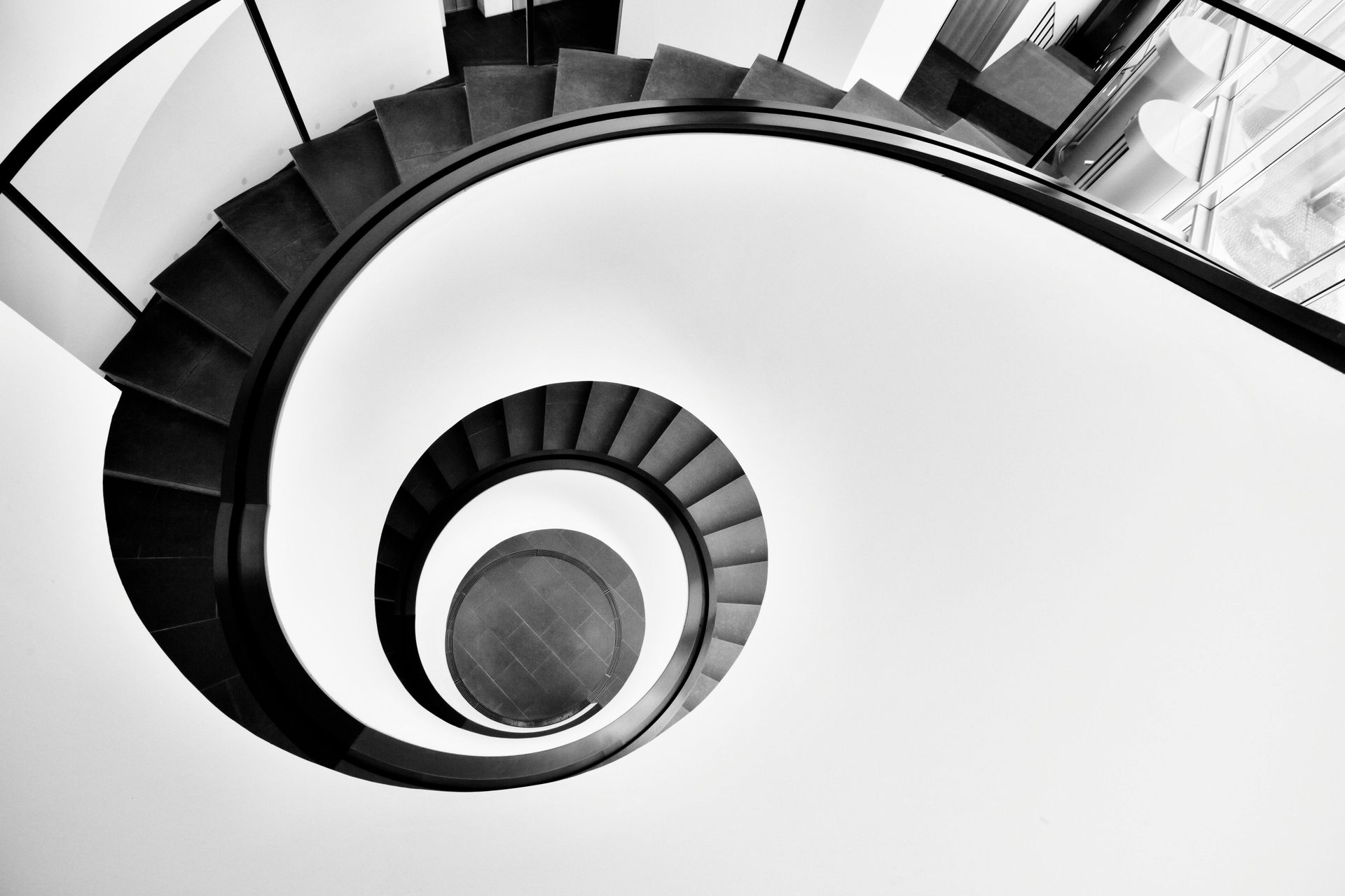 Escalera de caracol en blanco y negro, que se curva hacia abajo hasta un punto central.