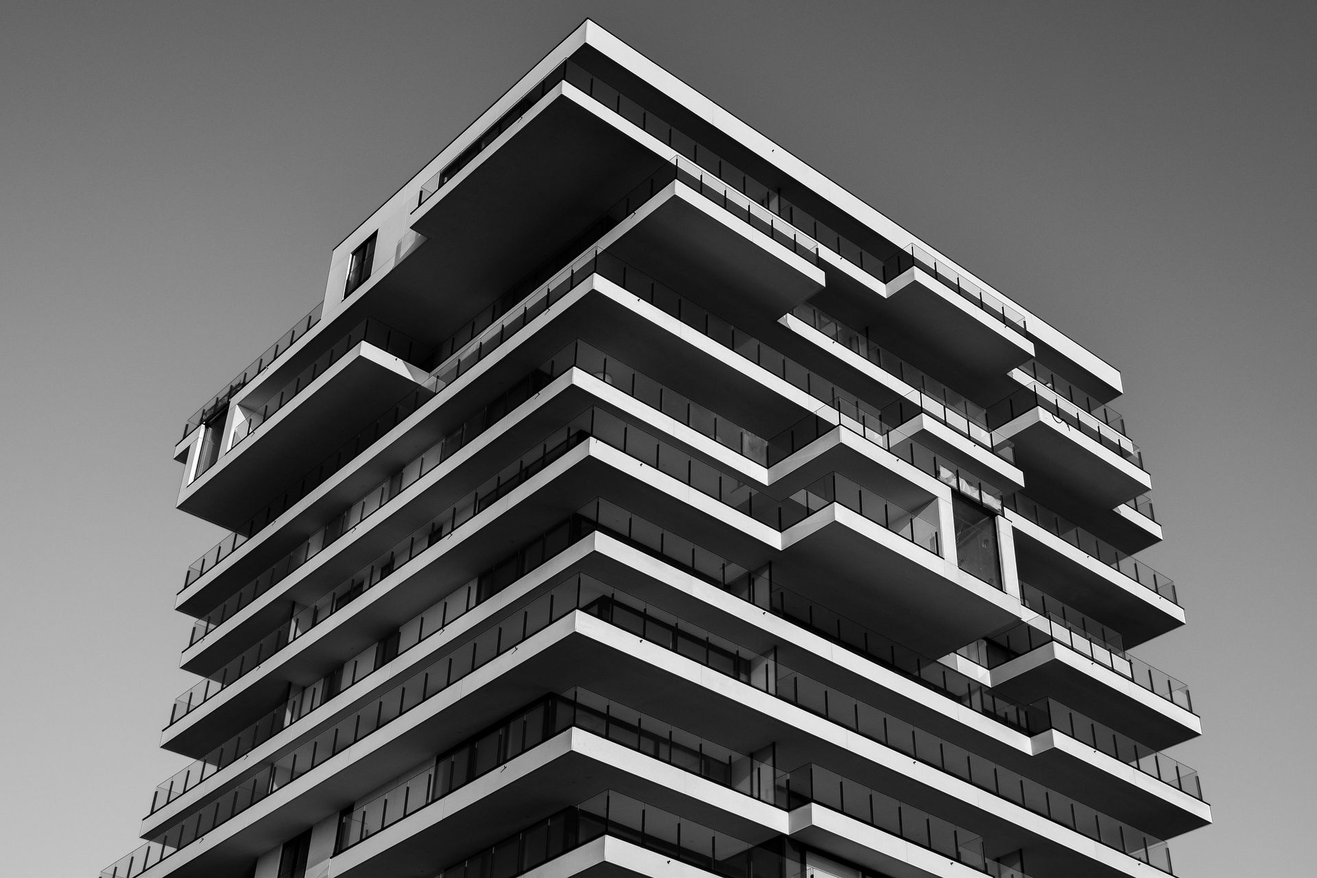 Fotografía en blanco y negro de un edificio moderno de gran altura con múltiples balcones, frente a un cielo despejado.