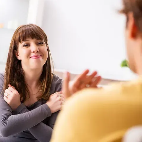 Mujer y hombre se comunican mediante lenguaje de señas; la mujer sonríe mientras hace la seña con los brazos cruzados.