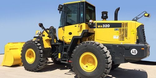 Cargador frontal Komatsu WA320 amarillo estacionado sobre una superficie de color claro con un fondo de cielo azul.