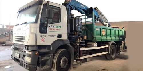 Un camión volquete blanco y verde con una grúa estacionado sobre una superficie pavimentada.