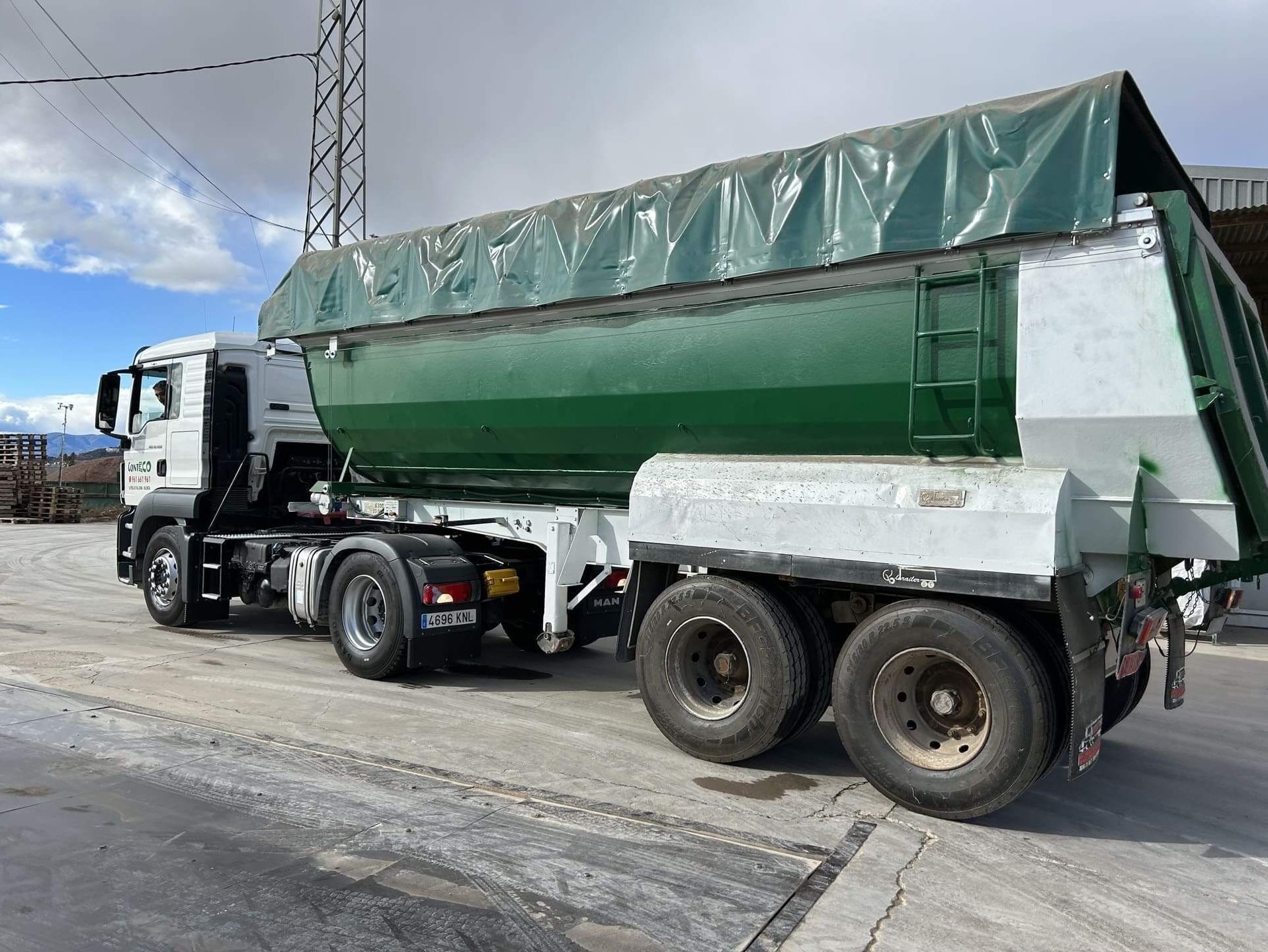 Camión blanco con caja de carga verde cubierta por lona, ​​estacionado al aire libre.