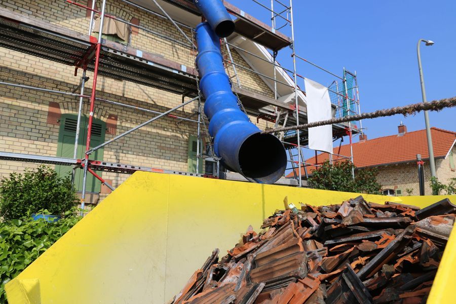 Un conducto azul cubre un contenedor amarillo lleno de escombros de madera en una obra de renovación de un edificio.