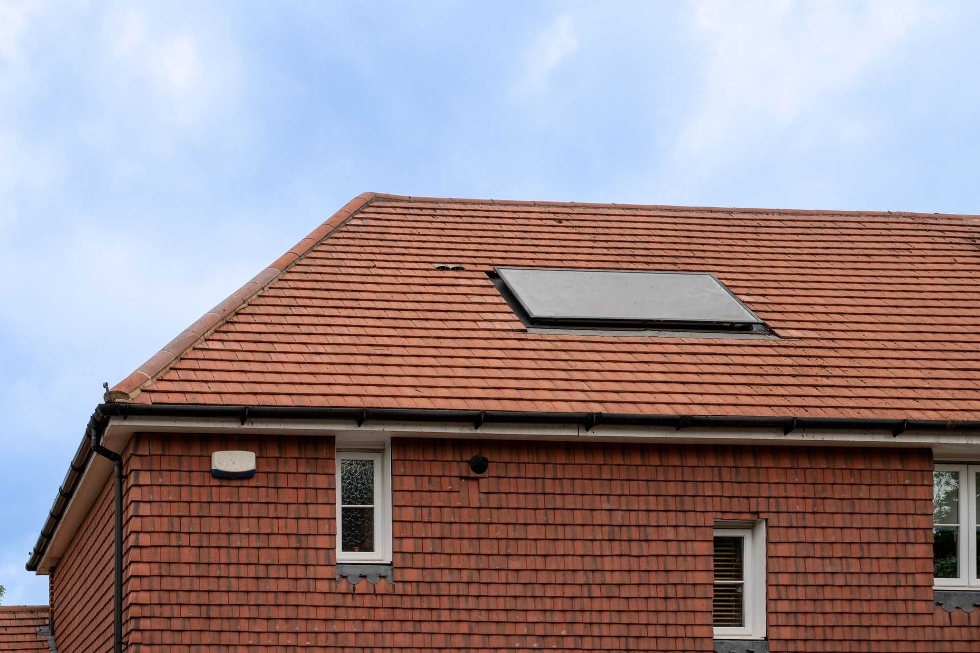 Red-tiled house roof with a skylight under a blue sky