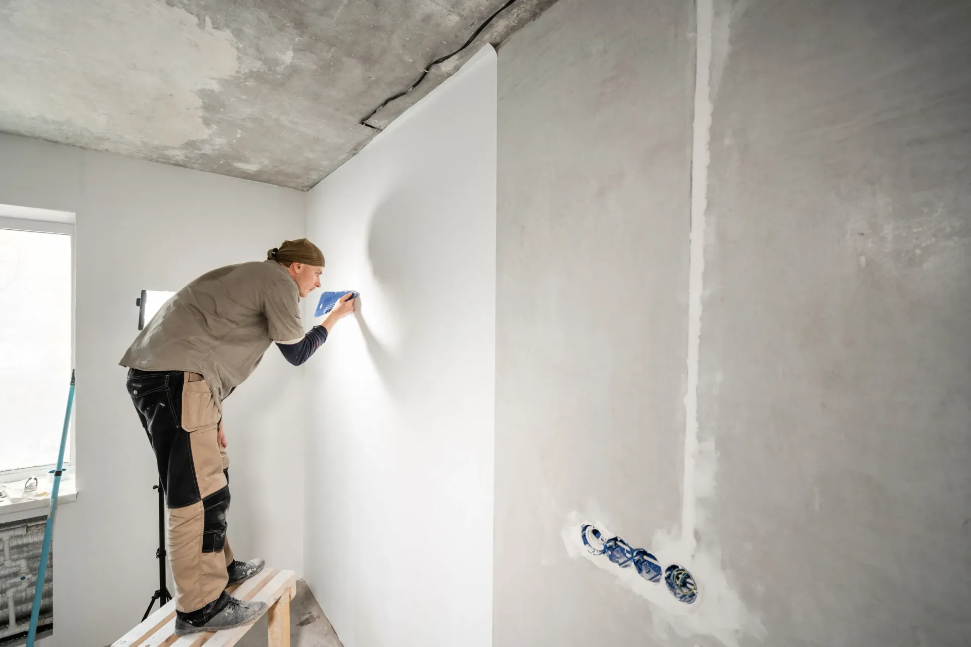 Persona en un taburete aplicando yeso a una pared interior con una llana. Habitación en construcción.