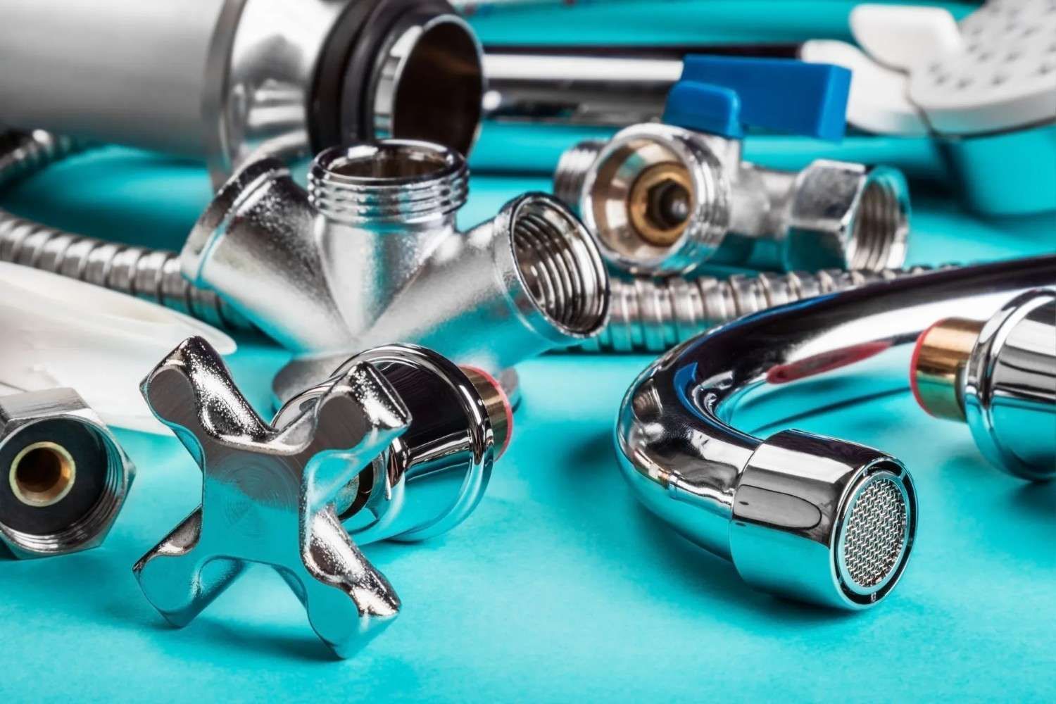 Accesorios de plomería y mangueras cromadas esparcidas sobre una superficie turquesa.