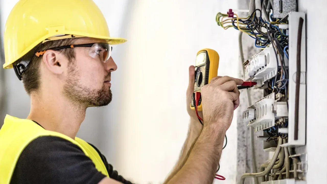 Técnico con casco amarillo utilizando un comprobador de voltaje en un panel eléctrico.