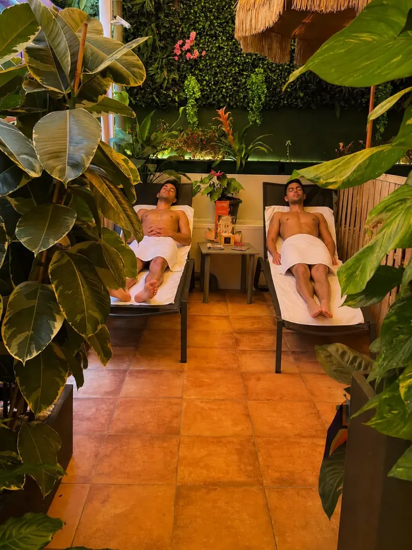 Dos personas se relajan en tumbonas en una sala de spa rodeada de vegetación y con un cálido suelo de baldosas.