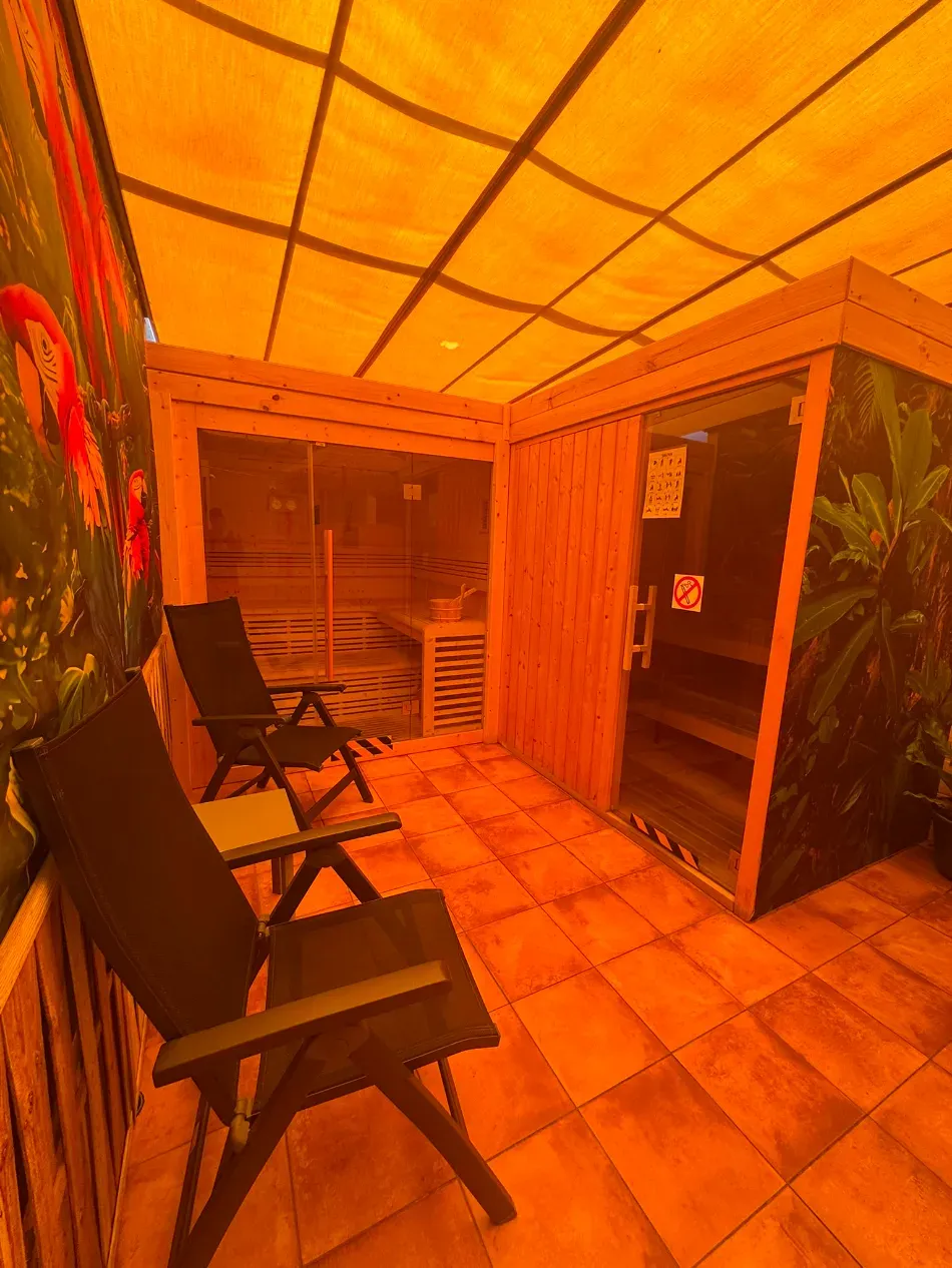 Sala de sauna iluminada con luz naranja, con sillas plegables y suelo de baldosas.