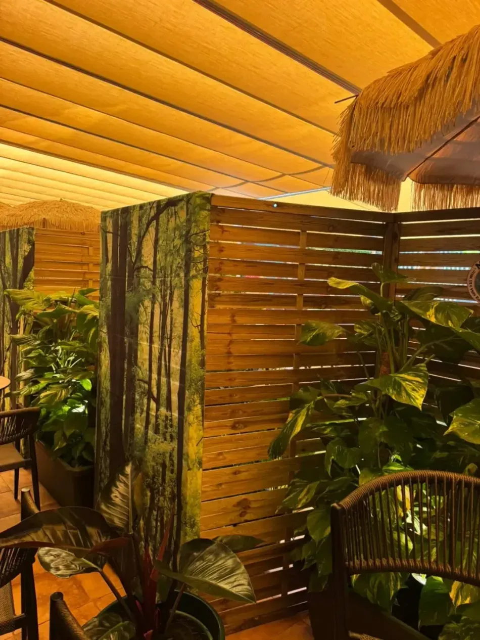 Patio tropical con listones de madera, exuberantes plantas verdes y sillas de mimbre bajo un cálido toldo.