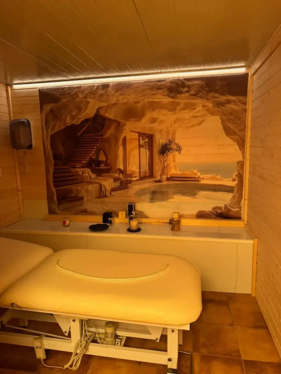 Camilla de masaje en una habitación alicatada con un mural de tonos cálidos como fondo e iluminación tenue.