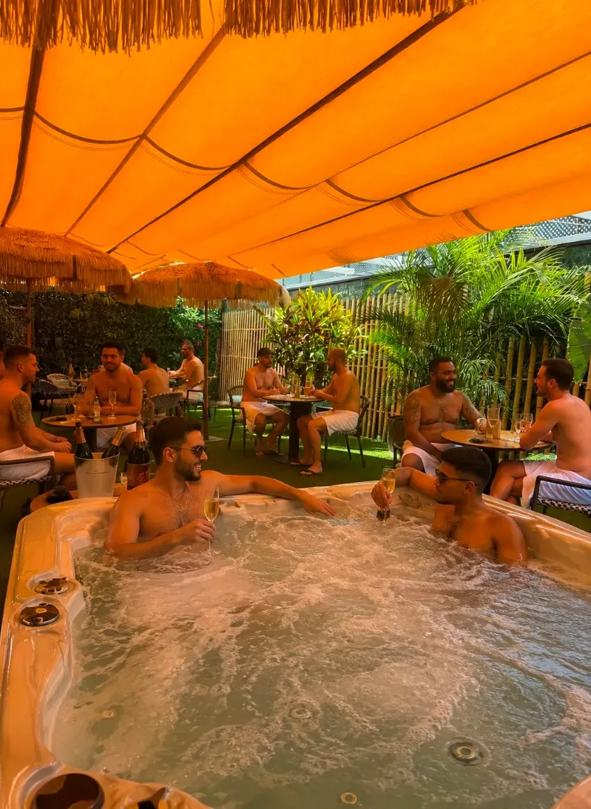 Personas relajándose en un jacuzzi bajo un toldo naranja en un entorno exterior exuberante.