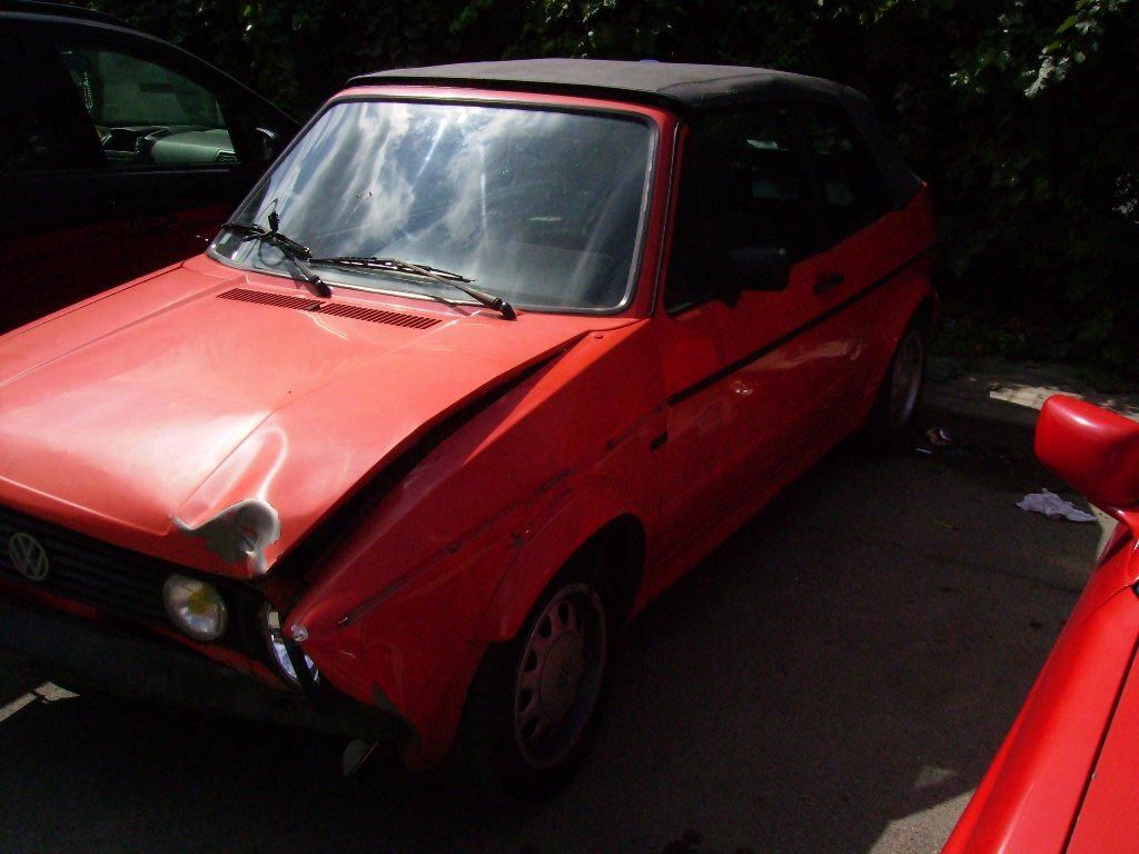 Coche descapotable rojo con daños en la parte delantera; aparcado en un lugar soleado al aire libre.