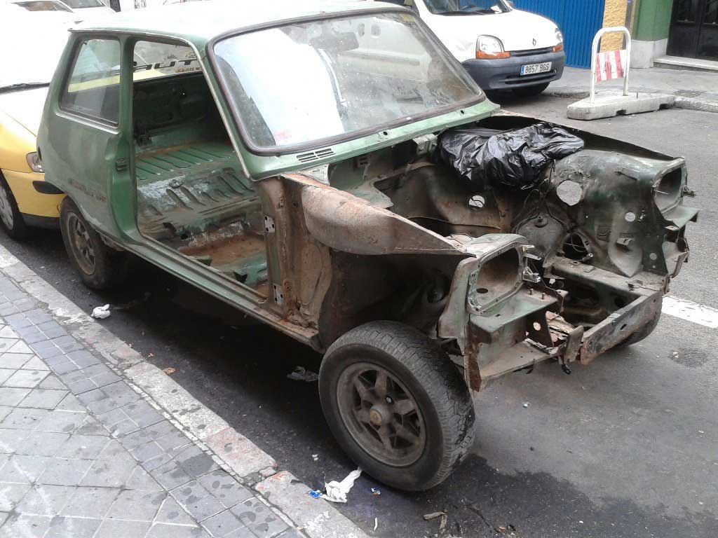 Un coche verde, parcialmente desmontado, aparcado en una calle de la ciudad.