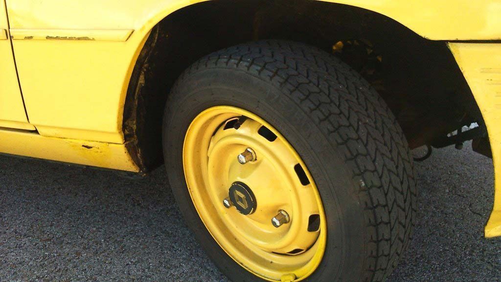 Rueda de coche amarilla sobre asfalto. La rueda también es amarilla con un neumático negro.