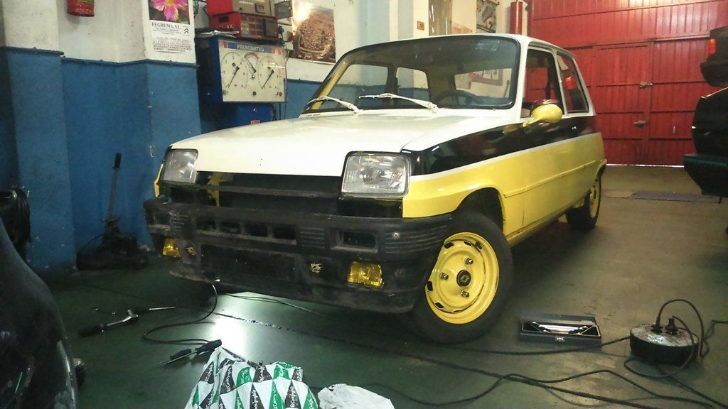 Renault 5 amarillo y blanco en un garaje; franja negra lateral; llantas amarillas y faros antiniebla.