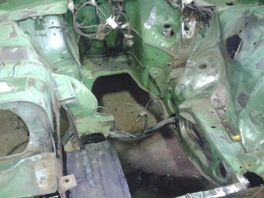 Compartimento del motor verde de un coche, parcialmente desmontado, con cableado y corrosión visibles.