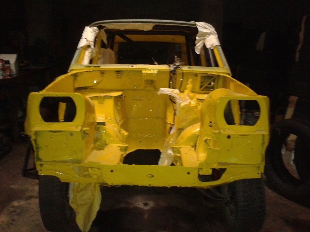 Chasis de coche amarillo, vista frontal, dentro de un garaje, en proceso de restauración.