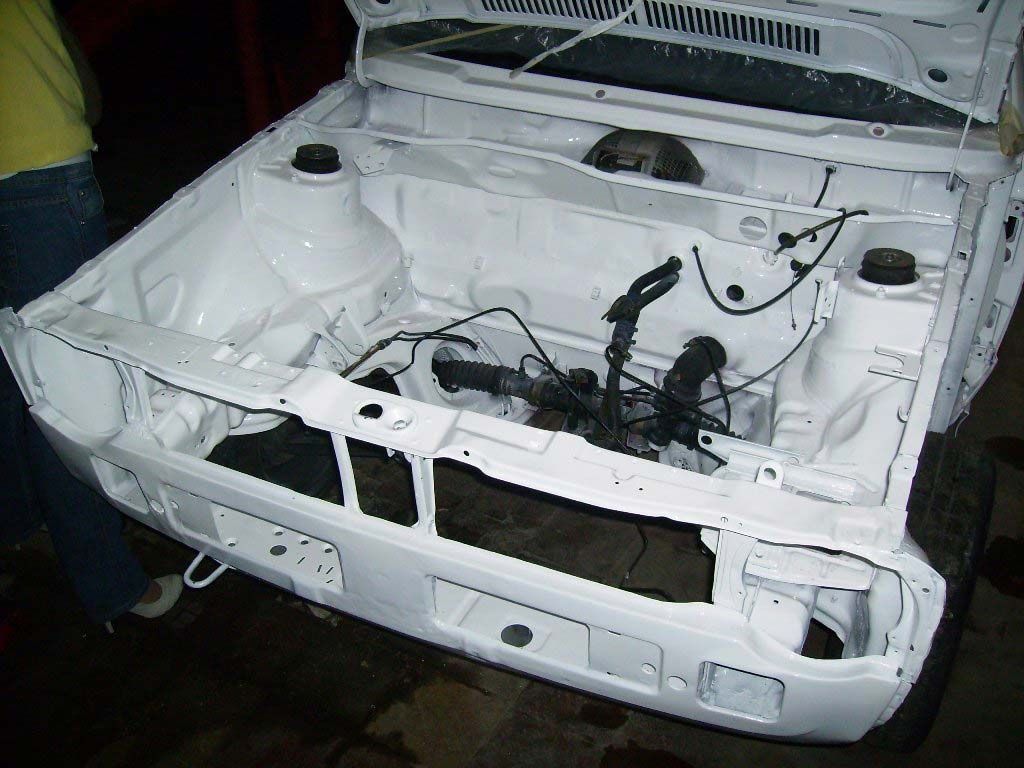 Compartimento del motor de un coche blanco, vista frontal, parcialmente desmontado.