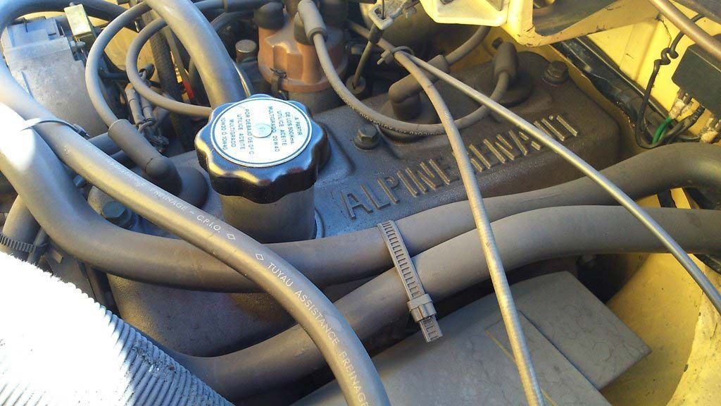 Motor de un vehículo con tapa de válvulas y mangueras del radiador negras, y tapón blanco y negro.