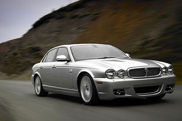 Un Jaguar sedán plateado en una carretera, con una ladera desenfocada al fondo.