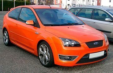 Un Ford Focus naranja aparcado en un estacionamiento, con llantas de aleación plateadas.