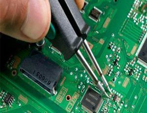 Mano utilizando pinzas para trabajar en una placa de circuito verde, reparando aparatos electrónicos.