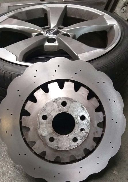 Conjunto de disco de freno y rueda. Disco plateado con orificios circulares y rueda radial. Neumático al fondo.