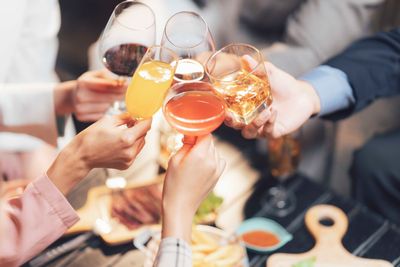 Hände stoßen mit Gläsern voller Wein, Cocktails und Säften an und feiern im Freien.