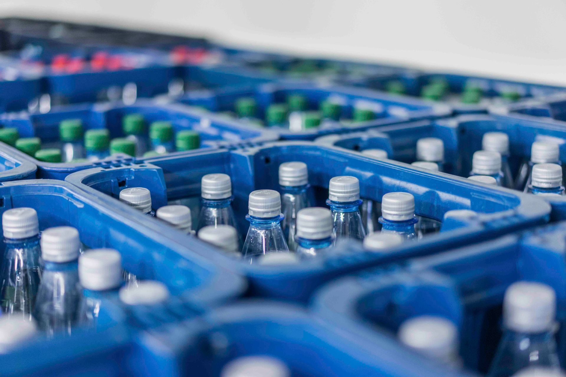 Getränke in Flaschen in blauen Plastikkisten, weiße und grüne Flaschenverschlüsse sichtbar.