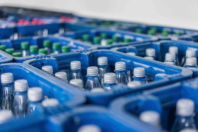 Getränke in Flaschen in blauen Plastikkisten, weiße und grüne Flaschenverschlüsse sichtbar.