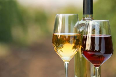 Zwei Weingläser, eines mit Weißwein, eines mit Rotwein, im Hintergrund eine Weinflasche.