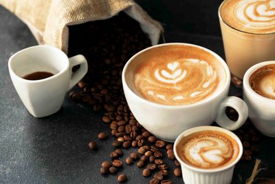 Kaffeetassen mit Latte Art, Kaffeebohnen und ein Jutesack auf dunklem Untergrund.