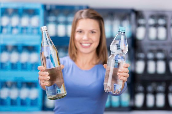 Frau in einem Geschäft, die ein Glas und eine Plastikwasserflasche hält und lächelt.