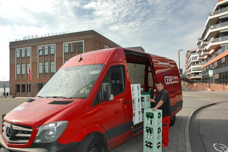 Ein Mann verlädt Bierkisten in einen roten Lieferwagen in einer städtischen Umgebung.