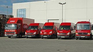 Fünf rote Lieferwagen parkten vor einem weißen Lagergebäude.