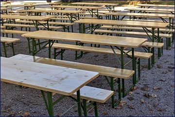 Leere hölzerne Picknicktische und Bänke, draußen auf einer Kiesfläche aufgestellt.