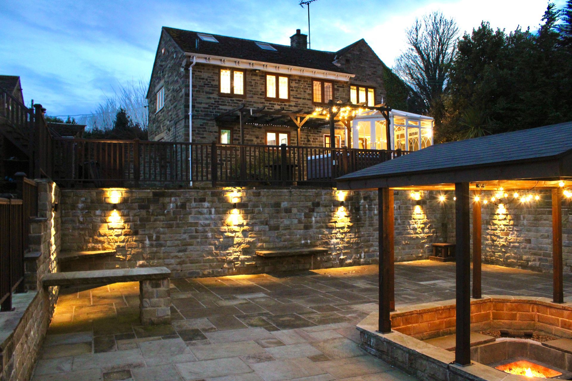 Habberjam farm Stone house and patio illuminated at dusk with built-in bench, pergola, and fire pit.