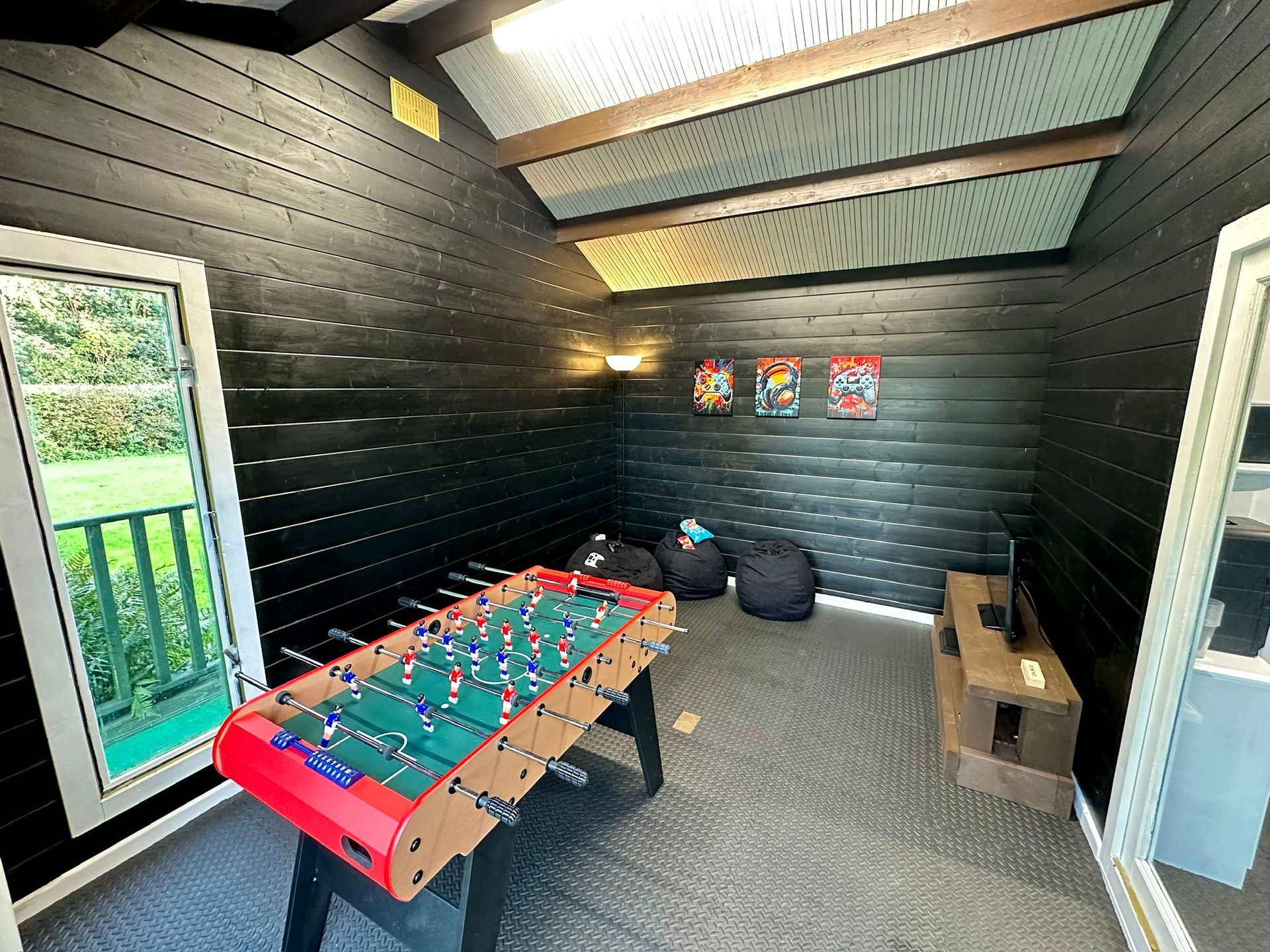 Foosball table in a black-walled game room. Windows on the sides, bean bags, and wall art visible.